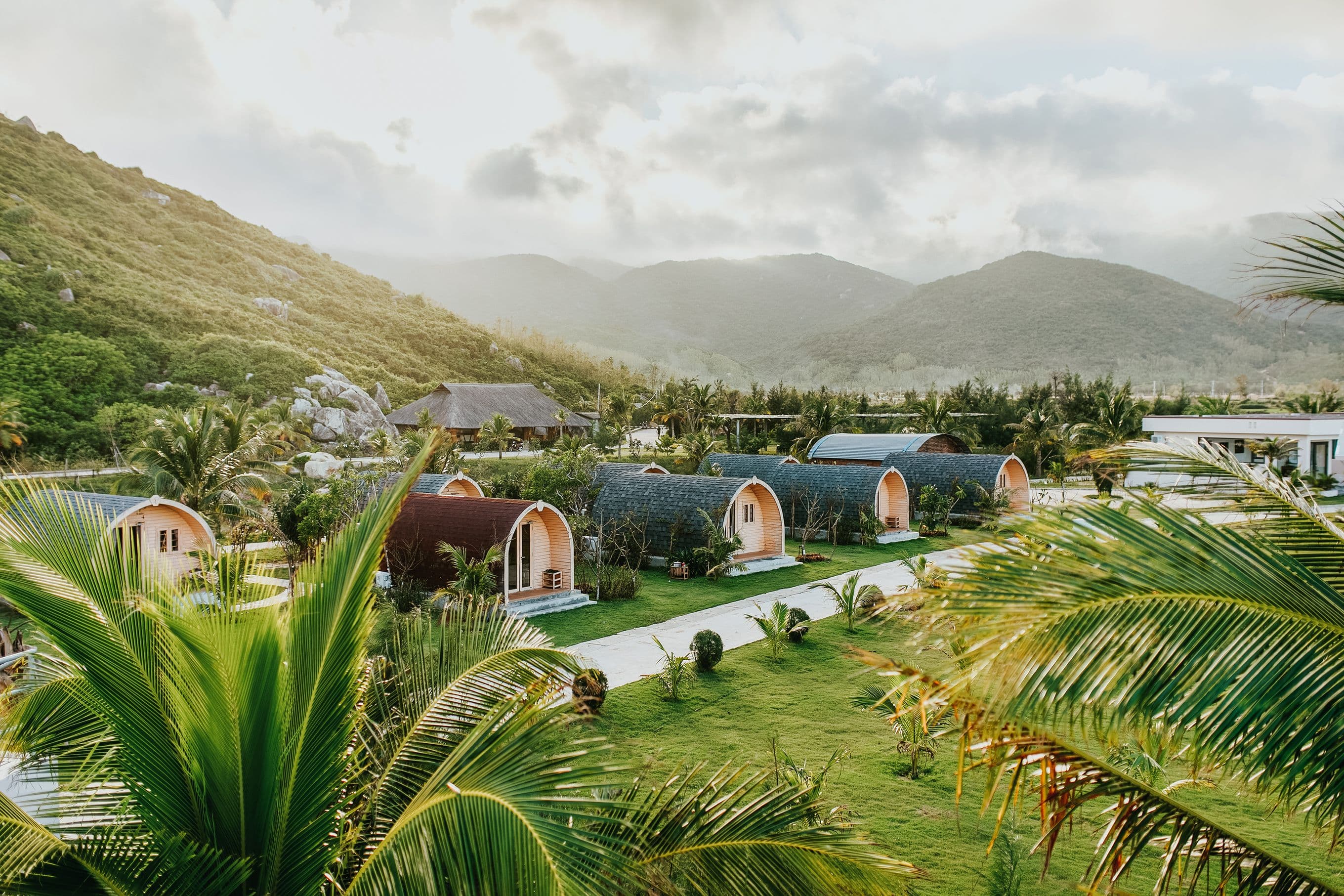 Arched villas at a hillside tropical resort framed by palm fronds and mountains